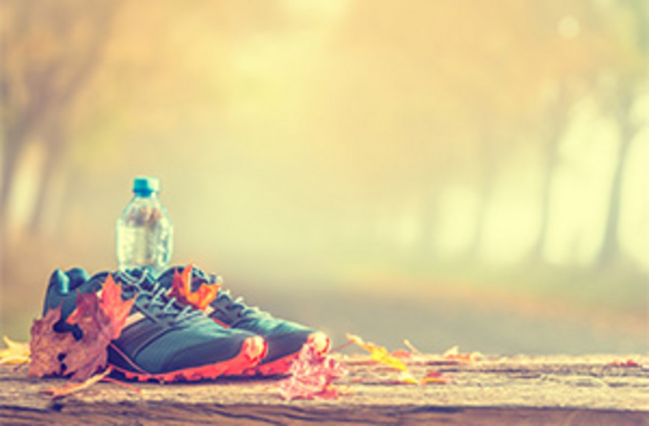 Laufschuhe und Trinkflasche vor nebliger Allee